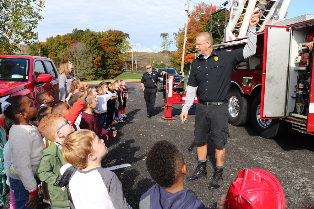 A firefighter stands in front of a fire truck with students