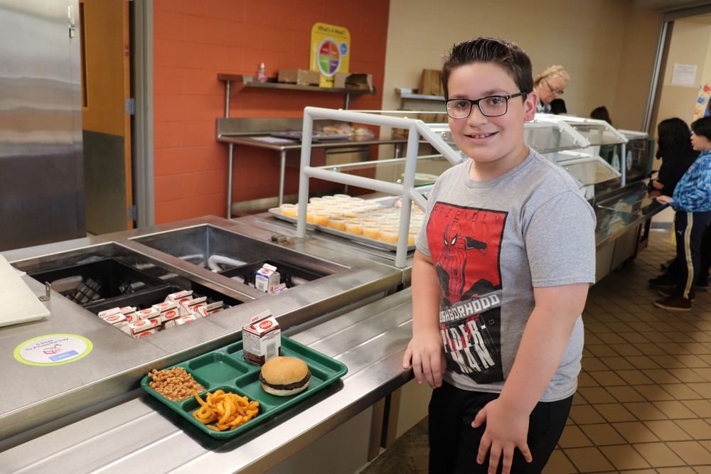 A student stands on line with his lunch tray